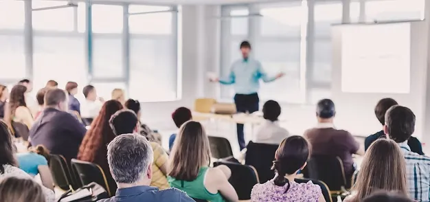 A person standing in front of a group of seated individuals, giving a presentation.
